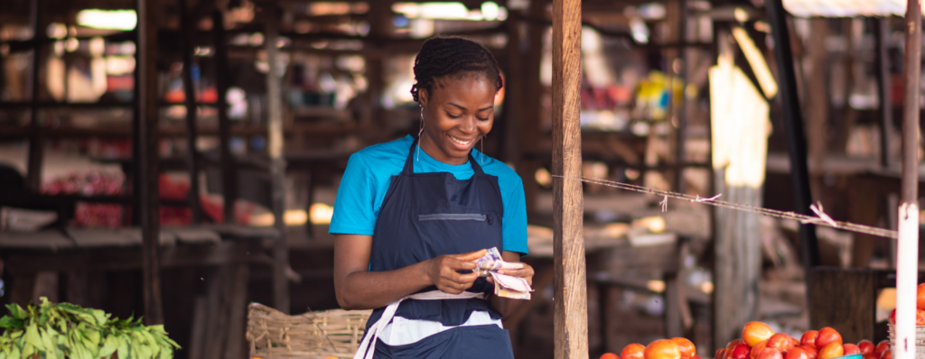 A young, pleased tomato seller is at her stall counting the money she got via her Renmoney loan